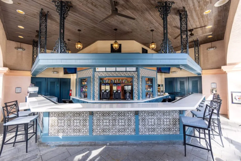 Port Orleans French Quarter open Bar with high top chairs along the sides. The refurbished color scheme is light blue and white with white tiles accented with black designs.